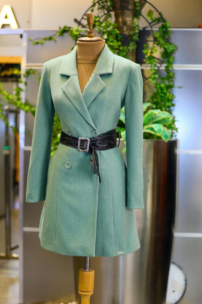 Stylish green coat displayed on a mannequin in a modern boutique setting.