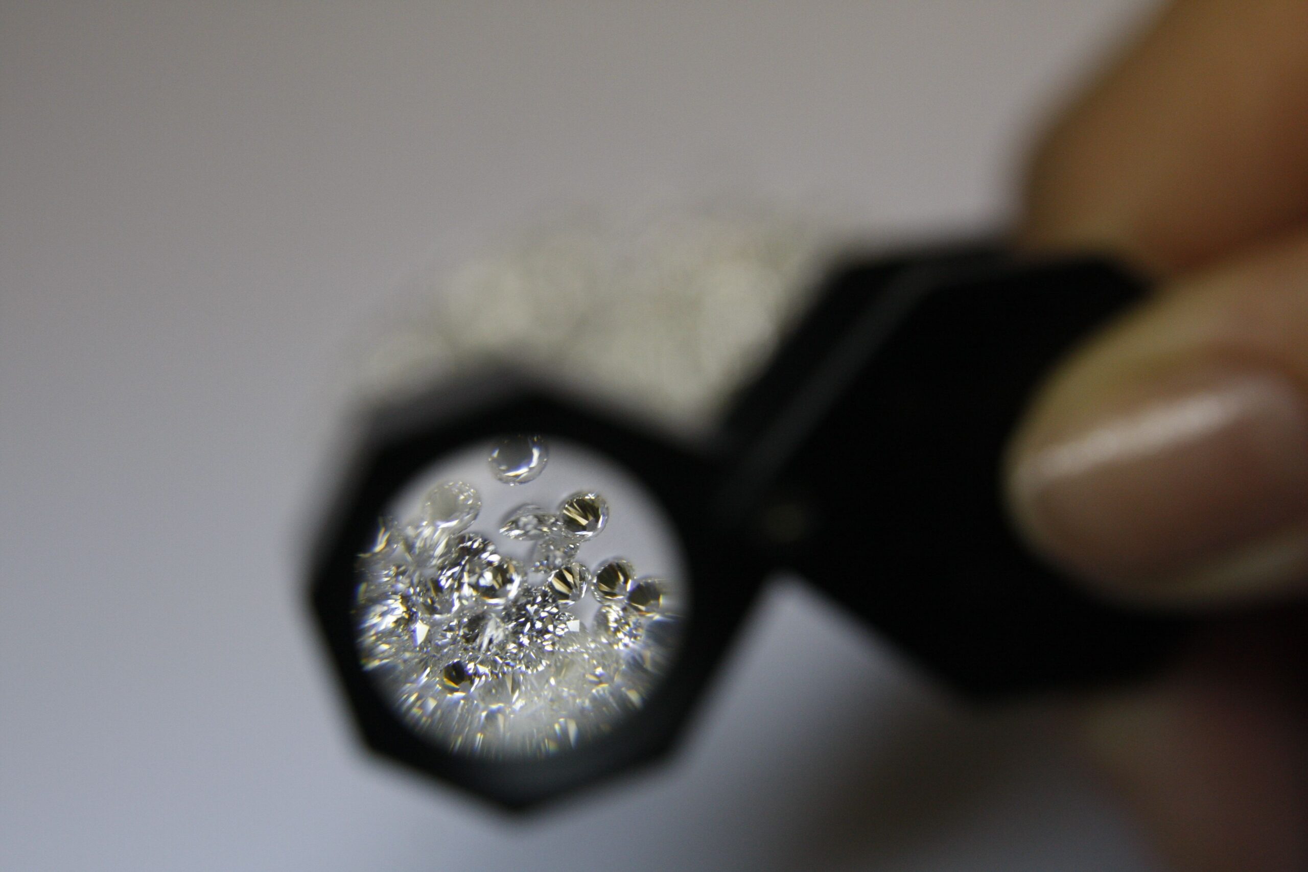 From above closeup of crop anonymous female jeweler with magnifying glass and diamonds in workshop